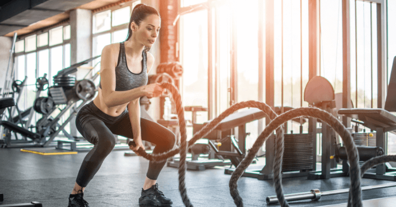 A woman using battle ropes in the gym early in the morning